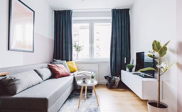 Imagem da sala de um apartamento pequeno com sofá, mesa, TV e rack