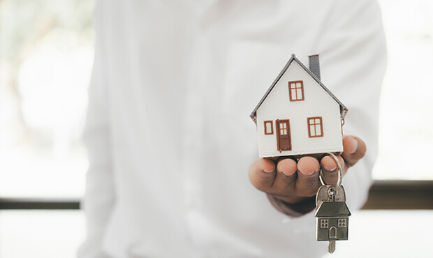 Imagem de uma pessoa mostrando uma miniatura de casa e uma chave