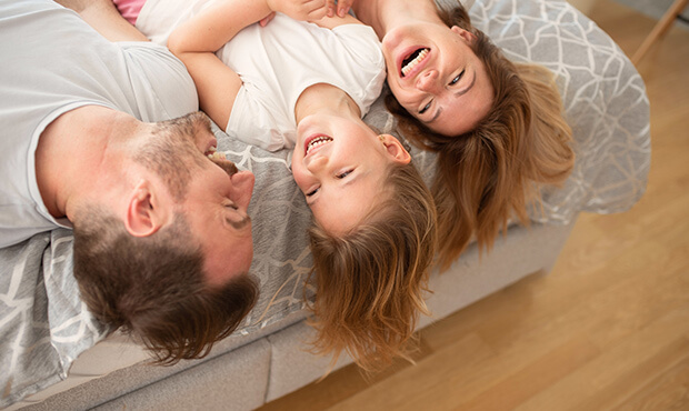 Imagem de uma mulher, um homem e uma criança rindo enquanto estão deitados na cama