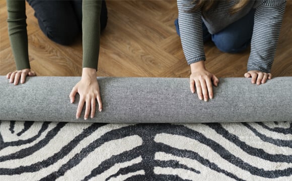 Imagem de duas pessoas desenrolando um tapete para sala