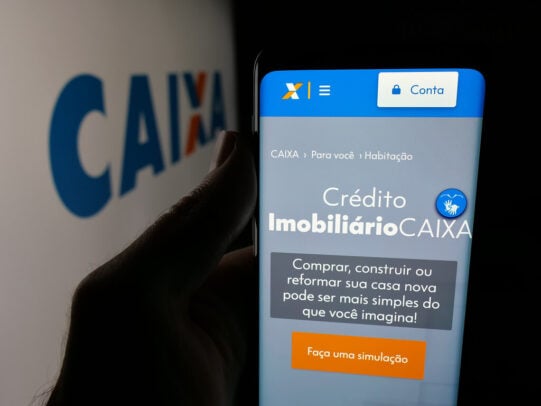 Celular exibindo página de crédito imobiliário da CAIXA com opção de simulação para financiamento habitacional.