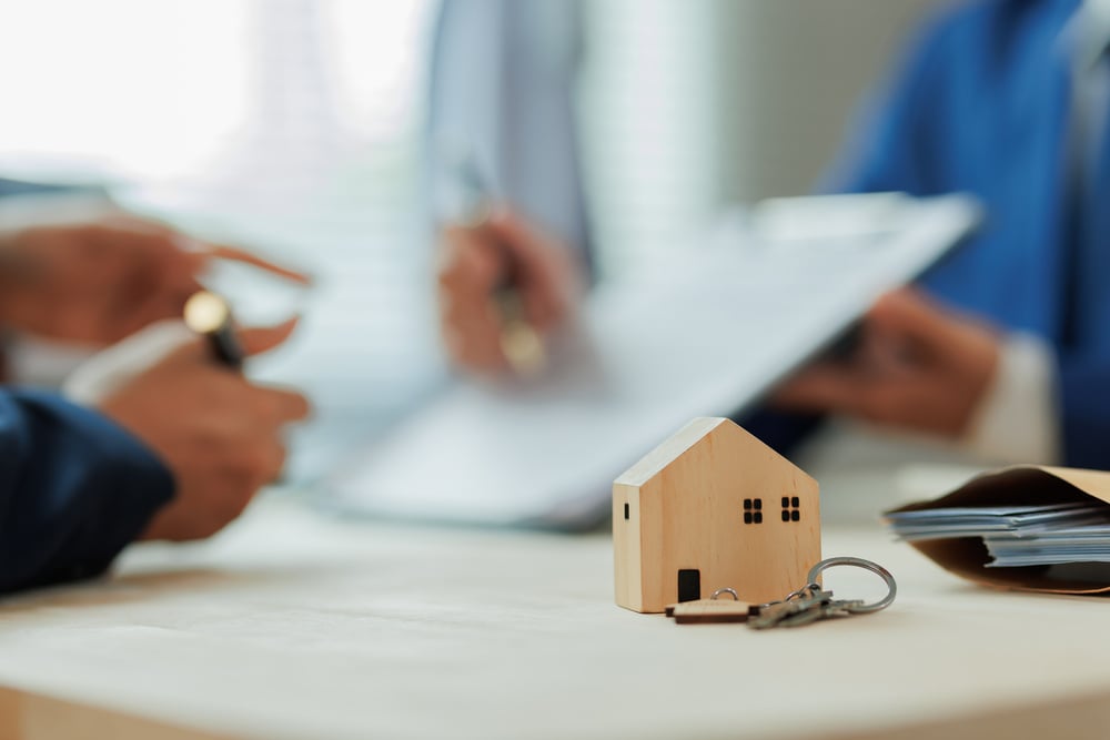 Um agente imobiliário explica as taxas de juros e os detalhes do contrato de compra de uma casa para um cliente, ajudando-o a entender os termos financeiros antes de comprar um imóvel