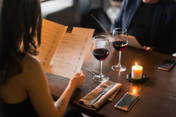 Casal apreciando taças de vinho e escolhendo pratos em cardápio elegante, cenário típico dos melhores restaurantes de Curitiba