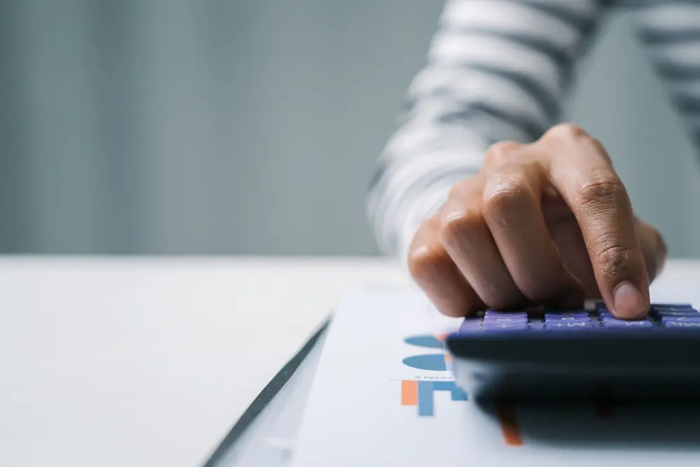 Pessoa usando calculadora para entender o que é ITBI e calcular custos na compra de imóvel, com gráfico financeiro ao fundo.