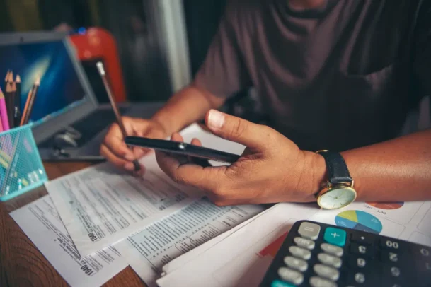 Pessoa analisando documentos e usando celular para entender o que é ITBI e calcular custos na compra de imóvel, com calculadora e papéis financeiros.