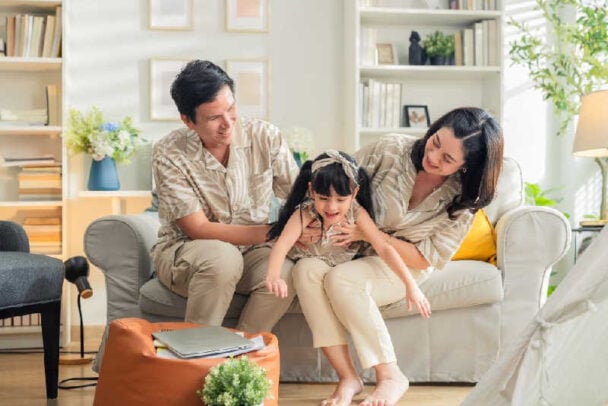 Família feliz com criança brincando na sala de estar, ilustrando o conforto do lar como parte essencial da qualidade de vida.