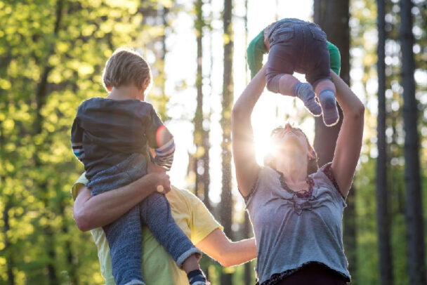 Pais brincando com seus filhos em um parque ensolarado, demonstrando a importância das relações familiares para uma excelente qualidade de vida.