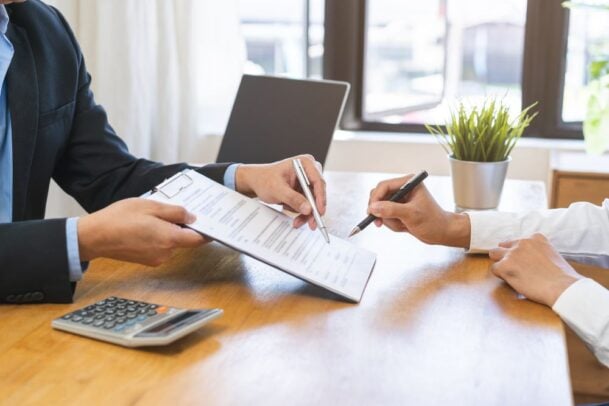 Pessoa assinando contrato de locação em mesa de escritório, representando o processo de análise de como funciona o seguro fiança.