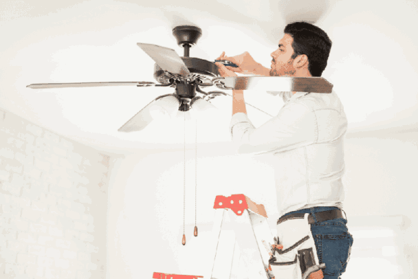 Homem em uma escada fixando uma das pás de um ventilador de teto marrom, ilustrando o processo de como instalar ventilador de teto