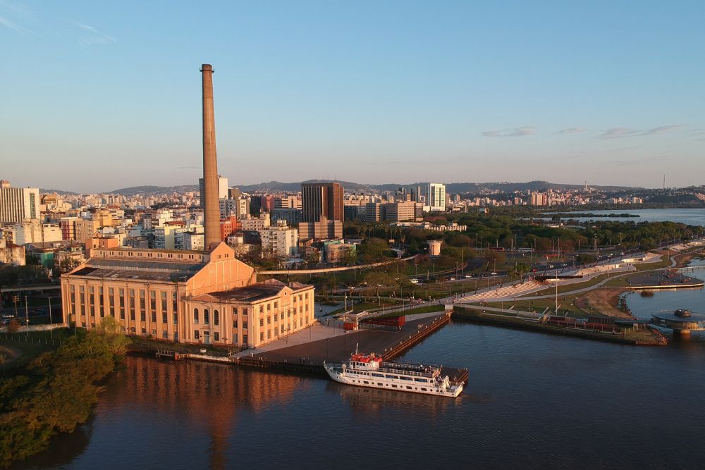 Pontos turísticos de Porto Alegre: Vista da Prefeitura Municipal (prédio sinuoso) e do Parque da Harmonia, com lago e ponte, na região central.