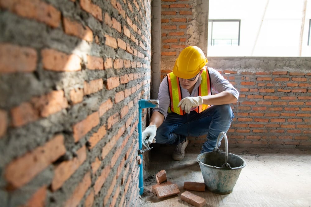 Trabalhador da construção aplica argamassa em parede de tijolos.