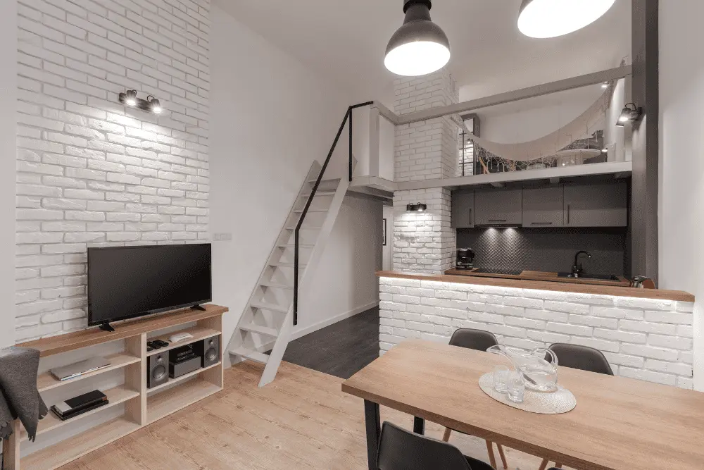 Apartamento estilo loft com mezanino sobre a cozinha e sala, acessado por escada e aproveitando o pé-direito alto.