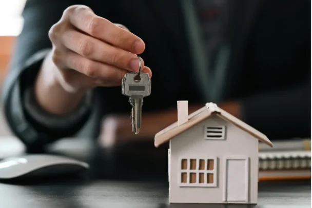 Pessoa segura chave acima de miniatura de casa, representando compra de imóvel e segurança jurídica garantida pelo operador nacional do sistema de registro de imóveis - onr.
