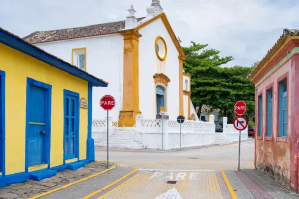 Rua histórica com casas coloridas e igreja colonial em Florianópolis. A cena representa o charme cultural da cidade ao abordar florianópolis custo de vida.