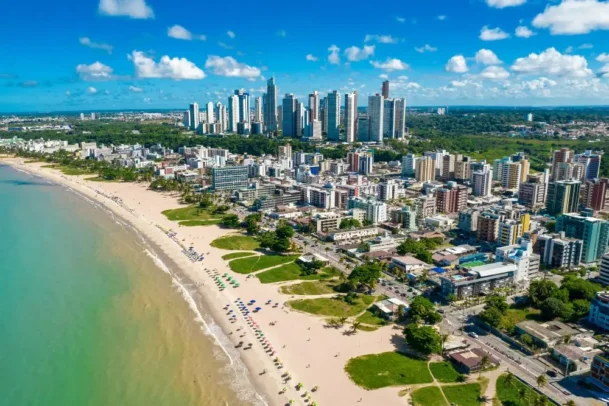 Vista aérea da orla de João Pessoa, uma das melhores cidades com praia para viajar no Nordeste, mostrando prédios e mar cristalino.