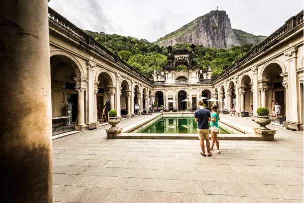 Visitantes no pátio histórico do Parque Lage, no Rio de Janeiro, com vista para o Cristo Redentor ao fundo, destino popular para quem busca o que fazer no rio de janeiro gastando pouco.