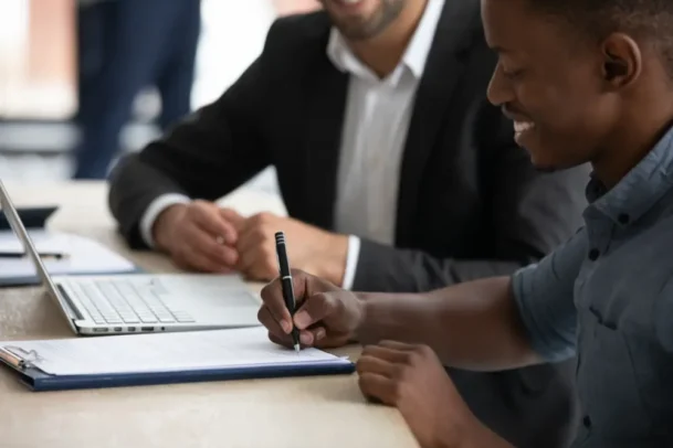 Cliente assinando documentos com apoio profissional durante negociação imobiliária, ilustrando orientações jurídicas e cuidados necessários para o cessionário de imóveis.